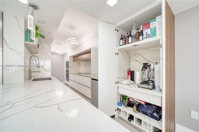 interior space featuring light stone countertops, decorative light fixtures, white cabinetry, and sink