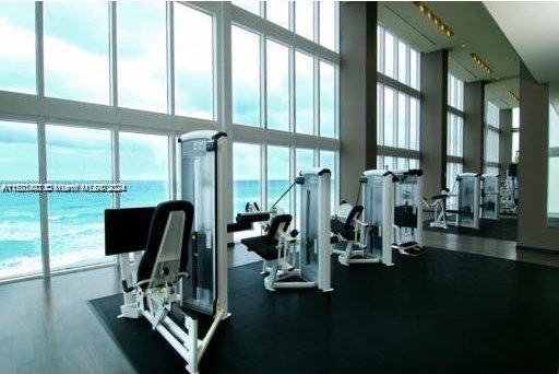 exercise room with floor to ceiling windows, a towering ceiling, and a water view