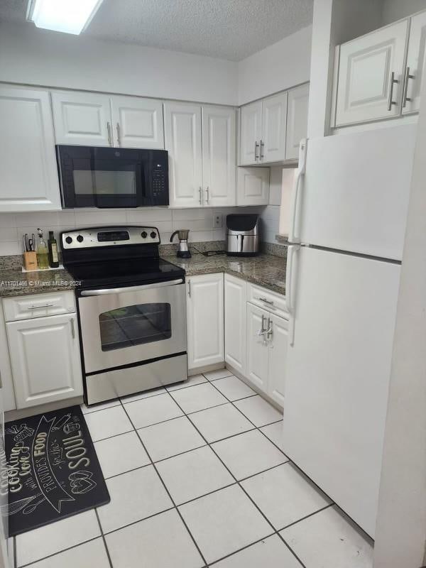 kitchen featuring a textured ceiling, electric range, white cabinets, white fridge, and light tile patterned flooring