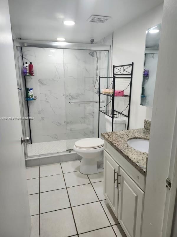 bathroom with toilet, vanity, tile patterned floors, and a shower with shower door