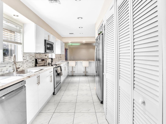 kitchen featuring decorative backsplash, marble finish floor, stainless steel appliances, white cabinetry, and a sink