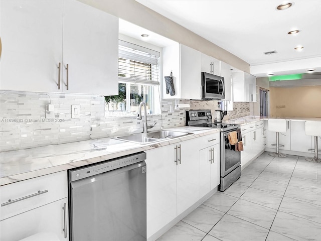 kitchen with a sink, white cabinetry, appliances with stainless steel finishes, decorative backsplash, and light stone countertops