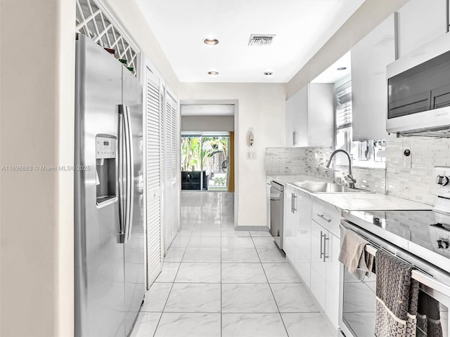 kitchen with stainless steel appliances, a sink, visible vents, white cabinetry, and tasteful backsplash