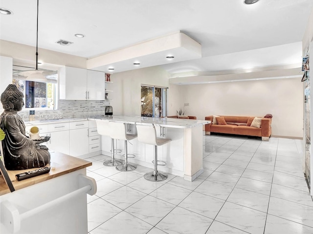 kitchen featuring visible vents, white cabinets, a breakfast bar, open shelves, and backsplash