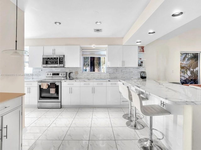 kitchen with a peninsula, appliances with stainless steel finishes, visible vents, and white cabinets