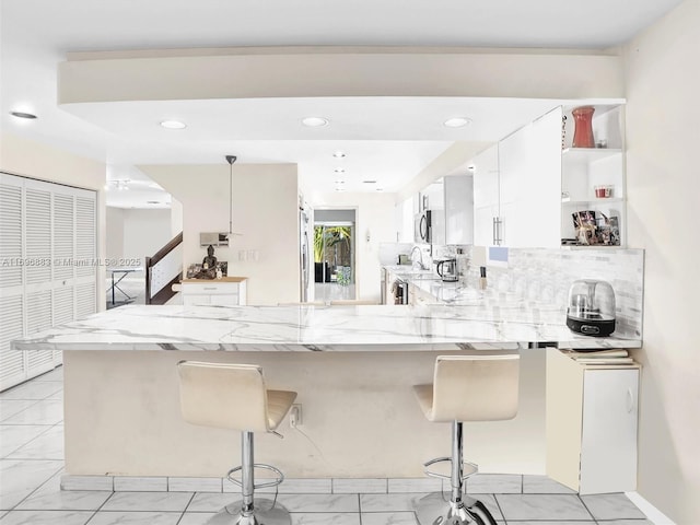 kitchen featuring backsplash, a peninsula, a breakfast bar area, and light stone countertops