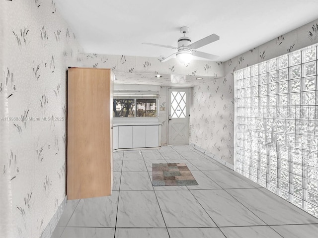 interior space with a ceiling fan and wallpapered walls