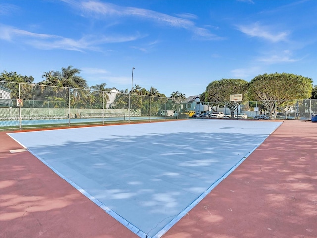 view of tennis court featuring community basketball court and fence