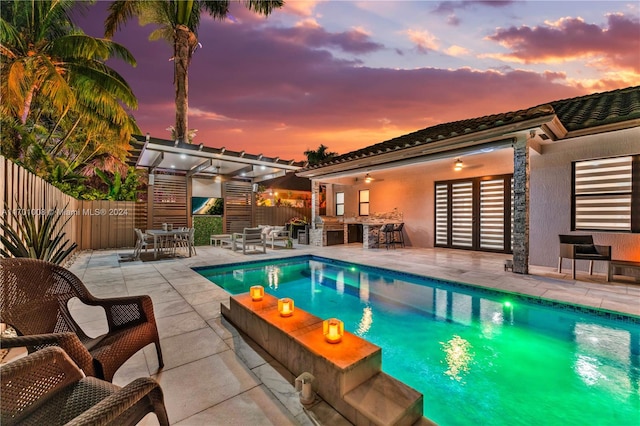 pool at dusk with exterior kitchen, an outdoor bar, a patio, and a pergola