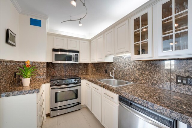 kitchen with appliances with stainless steel finishes, ornamental molding, sink, light tile patterned floors, and white cabinets