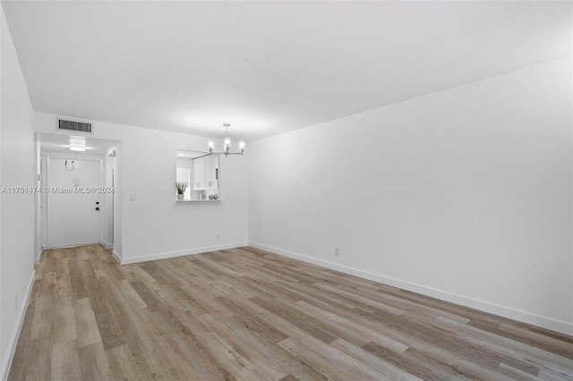 spare room with light hardwood / wood-style flooring and an inviting chandelier