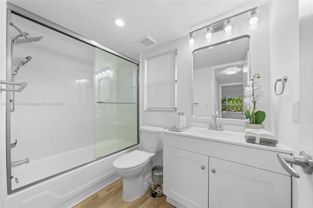 full bathroom with shower / bath combination with glass door, hardwood / wood-style floors, vanity, and toilet