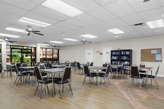 dining space with ceiling fan, a drop ceiling, and light wood-type flooring