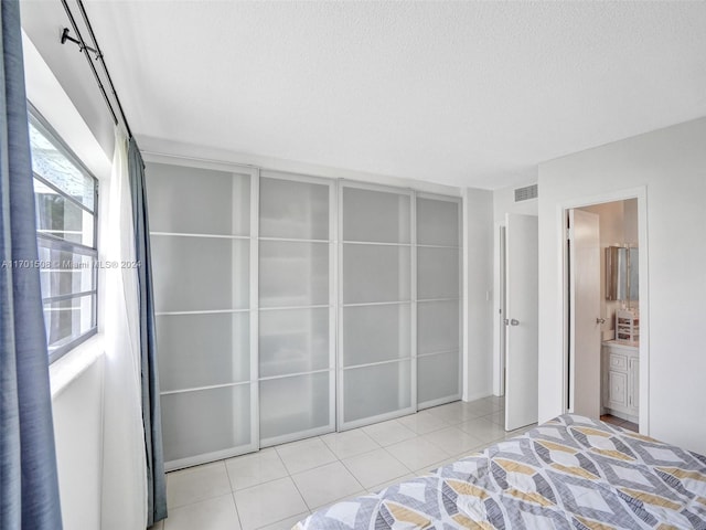 bedroom with ensuite bathroom, light tile patterned floors, and a textured ceiling