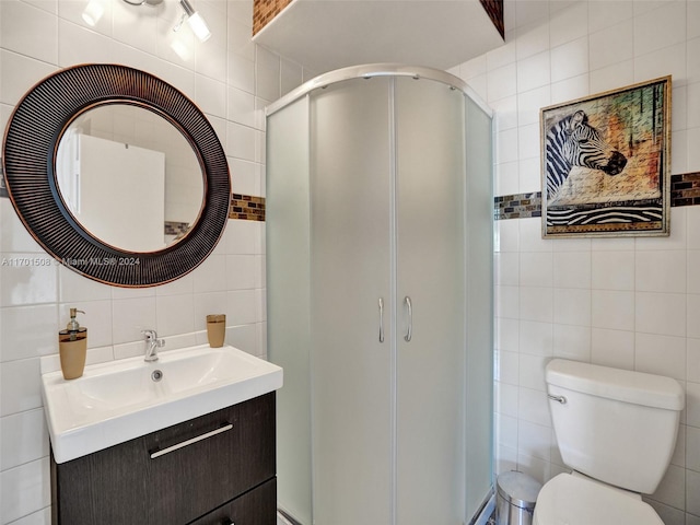 bathroom featuring vanity, toilet, a shower with shower door, and tile walls