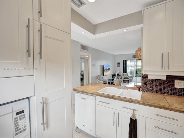 kitchen with dishwasher, sink, light tile patterned floors, tasteful backsplash, and white cabinetry