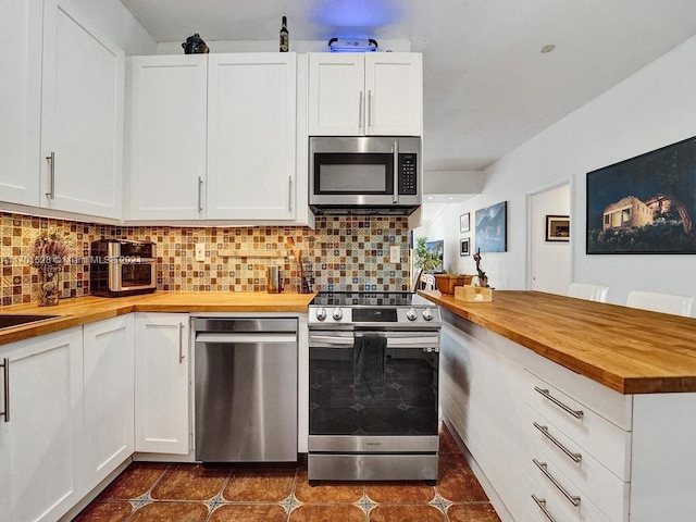 kitchen featuring butcher block counters, decorative backsplash, dark tile patterned floors, appliances with stainless steel finishes, and white cabinetry