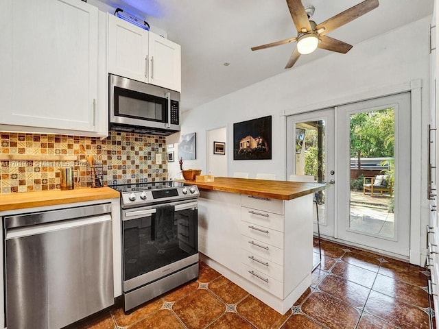 kitchen with wood counters, appliances with stainless steel finishes, french doors, tasteful backsplash, and white cabinets