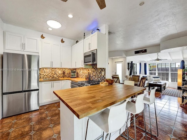 kitchen with backsplash, butcher block countertops, a kitchen bar, white cabinetry, and stainless steel appliances