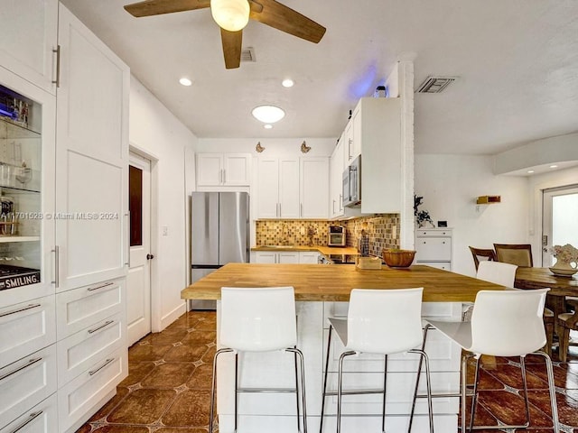 kitchen featuring a kitchen bar, stainless steel appliances, white cabinetry, and butcher block counters