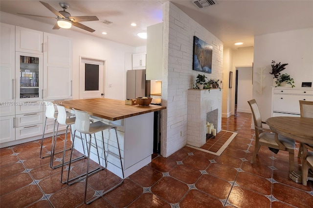 kitchen with white cabinets, a kitchen breakfast bar, butcher block countertops, and stainless steel fridge