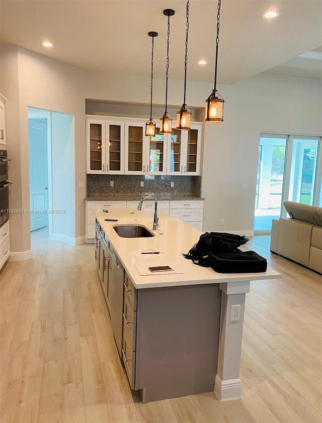 kitchen with light wood-type flooring, decorative light fixtures, white cabinetry, and a kitchen island with sink