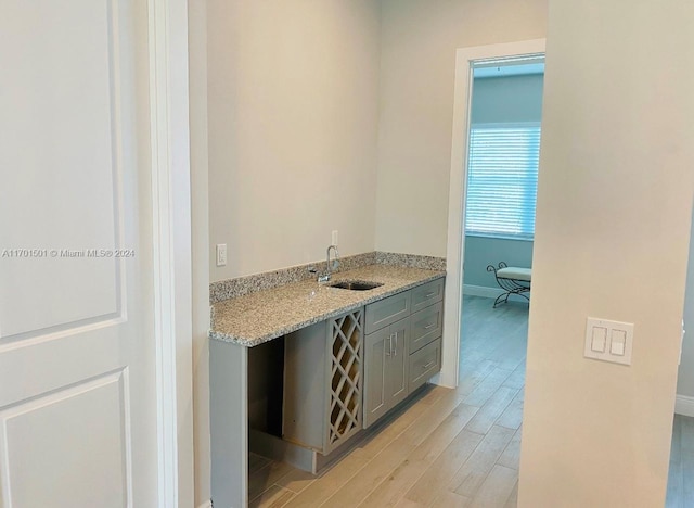 bar with gray cabinetry, light hardwood / wood-style floors, light stone countertops, and sink