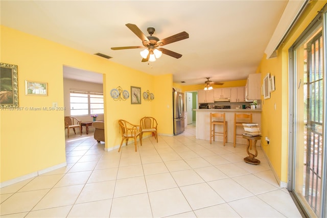 interior space featuring a kitchen breakfast bar, ceiling fan, light tile patterned floors, kitchen peninsula, and stainless steel refrigerator