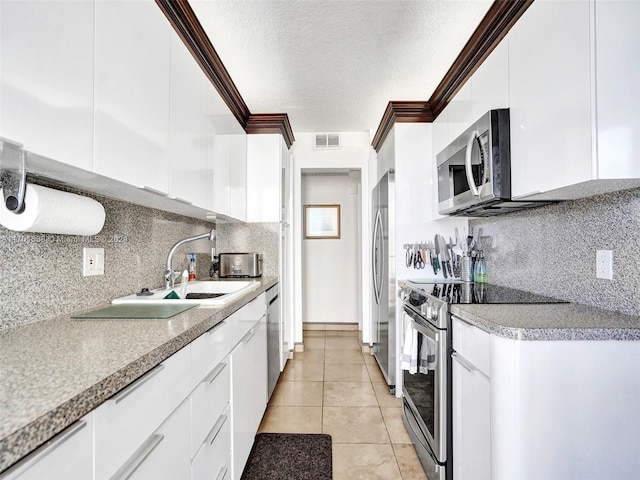 kitchen with appliances with stainless steel finishes, backsplash, ornamental molding, light tile patterned floors, and white cabinetry