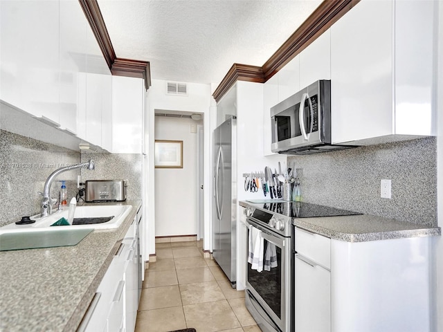 kitchen with sink, light tile patterned floors, a textured ceiling, white cabinets, and appliances with stainless steel finishes