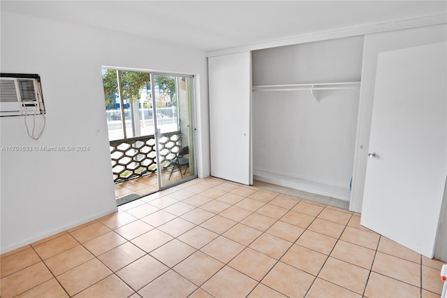 unfurnished bedroom featuring an AC wall unit, access to exterior, a closet, and light tile patterned flooring