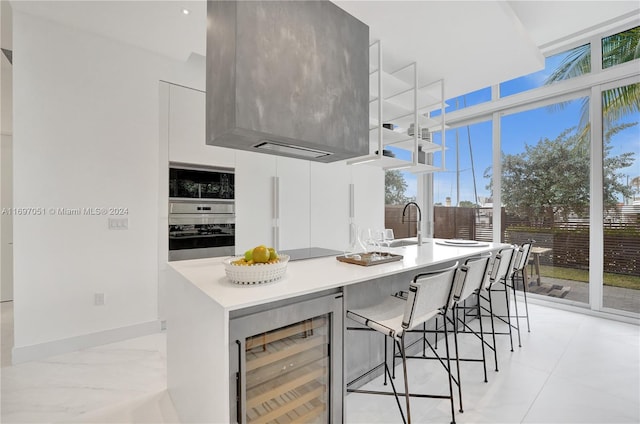 kitchen with wine cooler, a breakfast bar, white cabinets, black appliances, and a center island with sink