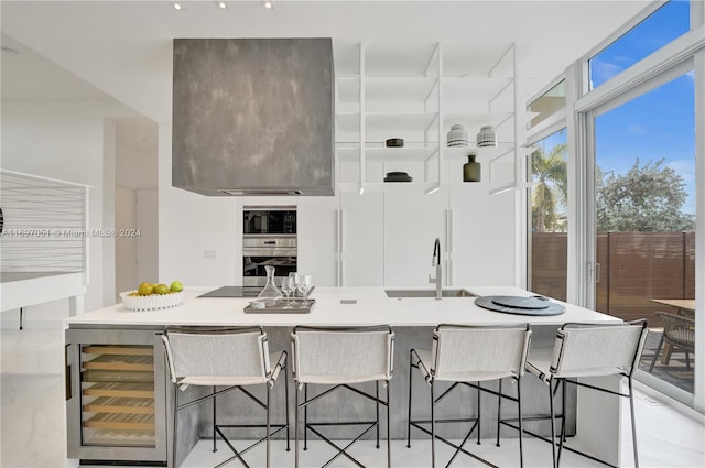 kitchen with a breakfast bar, sink, black appliances, wine cooler, and an island with sink