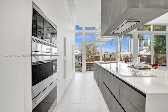 kitchen with stainless steel oven, floor to ceiling windows, black electric stovetop, sink, and light tile patterned floors