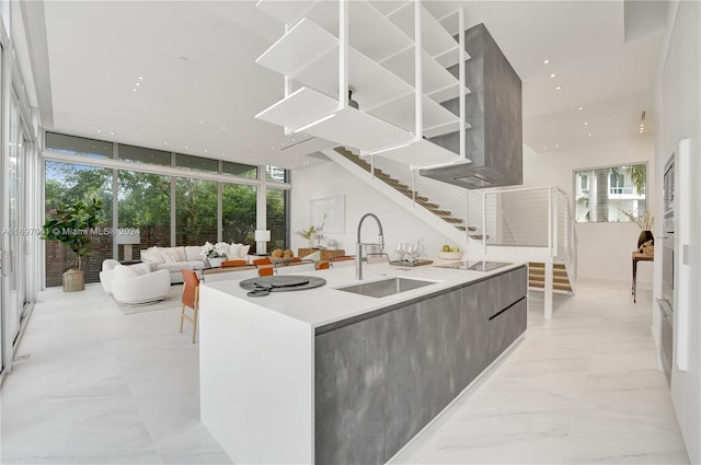 kitchen with a center island with sink, oven, expansive windows, black electric stovetop, and sink