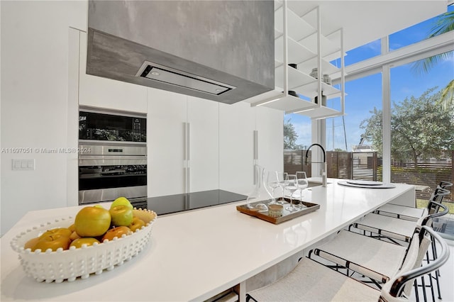 kitchen with white cabinets, stainless steel oven, ventilation hood, and a breakfast bar area