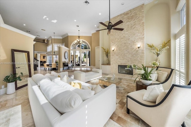 living room featuring ceiling fan with notable chandelier, ornamental molding, a fireplace, and a high ceiling