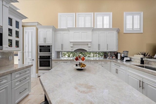 kitchen with white cabinets, light stone counters, sink, and double oven