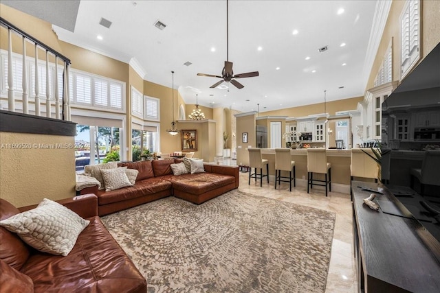 living room with ceiling fan, ornamental molding, and a high ceiling