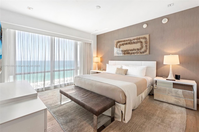 bedroom featuring access to exterior, light wood-type flooring, and a water view