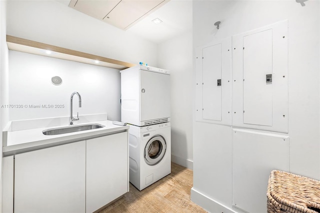 laundry room featuring stacked washer and clothes dryer, electric panel, sink, and light wood-type flooring