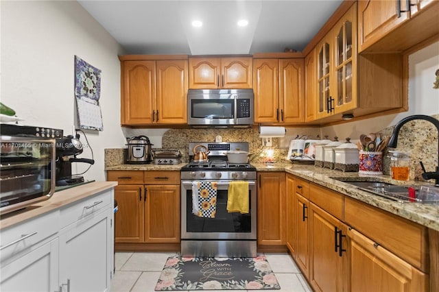 kitchen featuring appliances with stainless steel finishes, light stone counters, sink, light tile patterned floors, and white cabinets