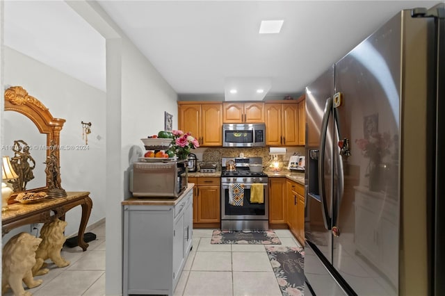 kitchen with light stone countertops, decorative backsplash, light tile patterned floors, and stainless steel appliances