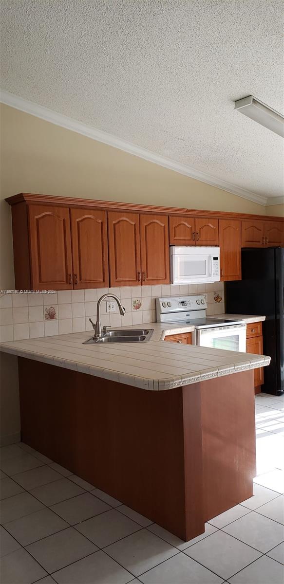 kitchen with sink, a textured ceiling, vaulted ceiling, white appliances, and ornamental molding