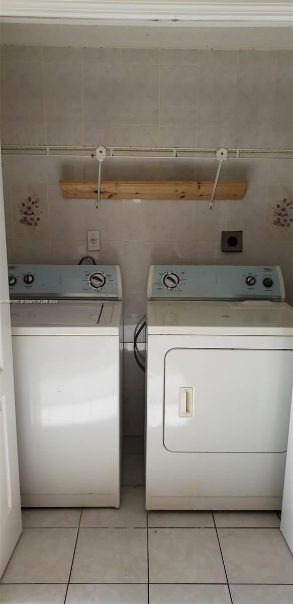 clothes washing area featuring washer and clothes dryer, light tile patterned flooring, and tile walls