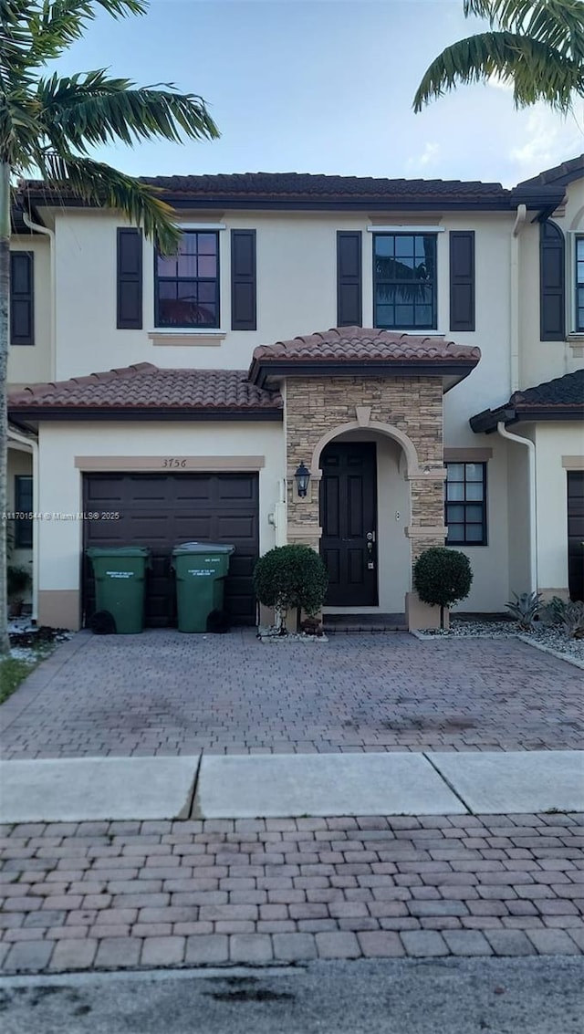 view of property featuring decorative driveway, stucco siding, a garage, stone siding, and a tiled roof