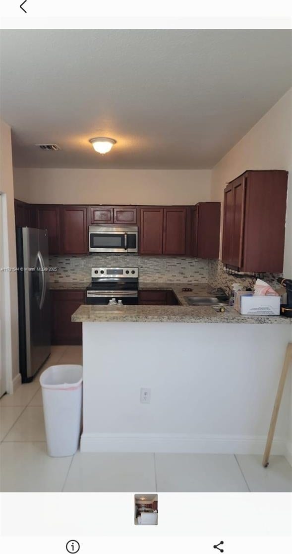 kitchen featuring light tile patterned floors, tasteful backsplash, appliances with stainless steel finishes, light stone counters, and a peninsula