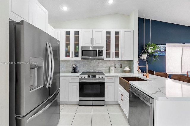 kitchen with white cabinets, sink, vaulted ceiling, light stone countertops, and appliances with stainless steel finishes