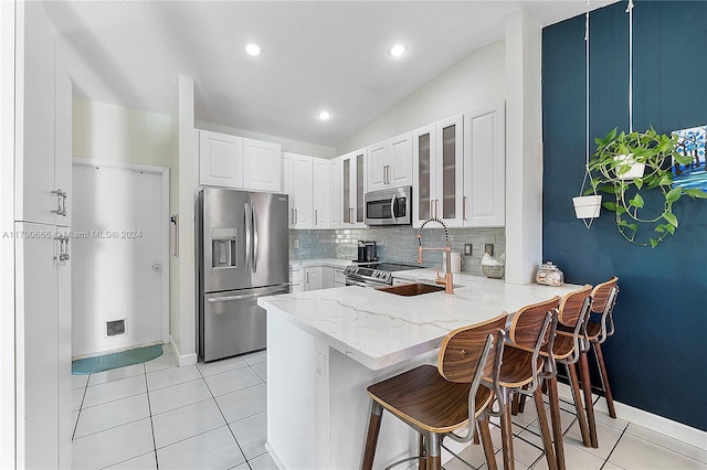 kitchen featuring white cabinets, kitchen peninsula, appliances with stainless steel finishes, and vaulted ceiling