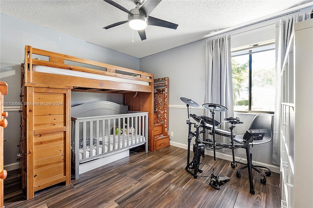 bedroom featuring a textured ceiling, ceiling fan, a crib, and dark wood-type flooring